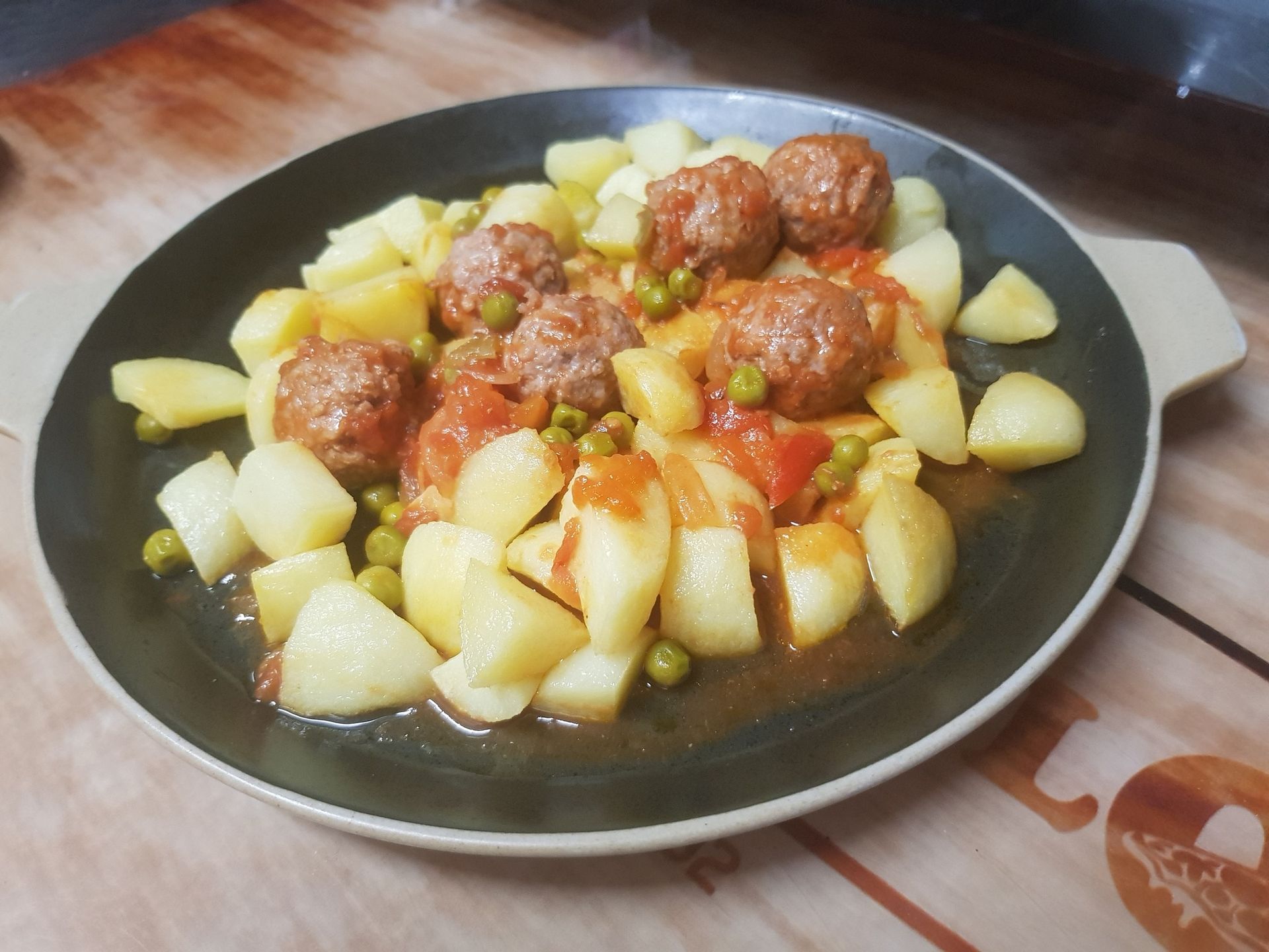 Albóndigas y patatas en salsa de tomate con guisantes, servidas en un plato oscuro.