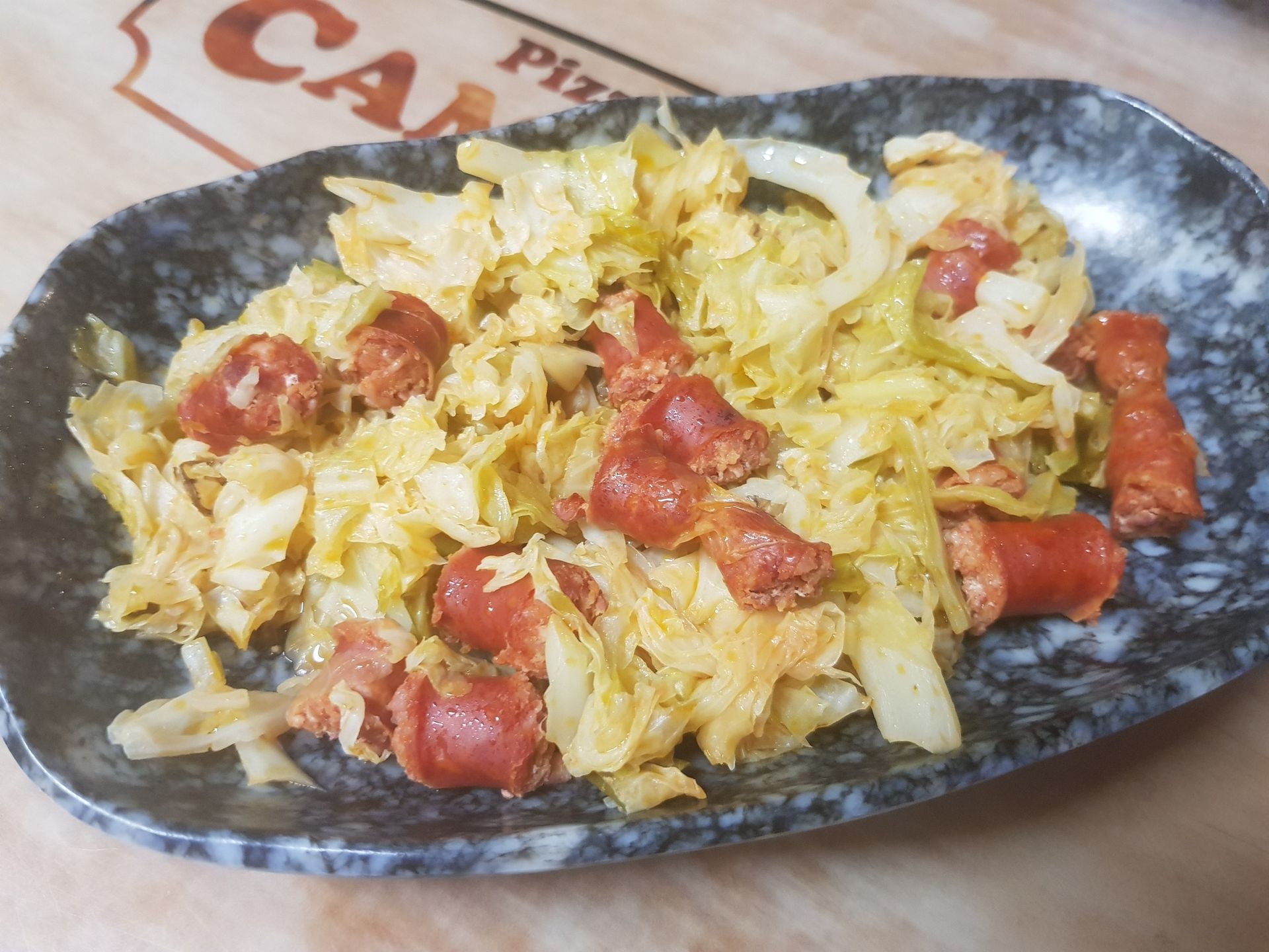 Plato de col y salchichas en un plato moteado de color gris; salchichas marrones y col amarilla.