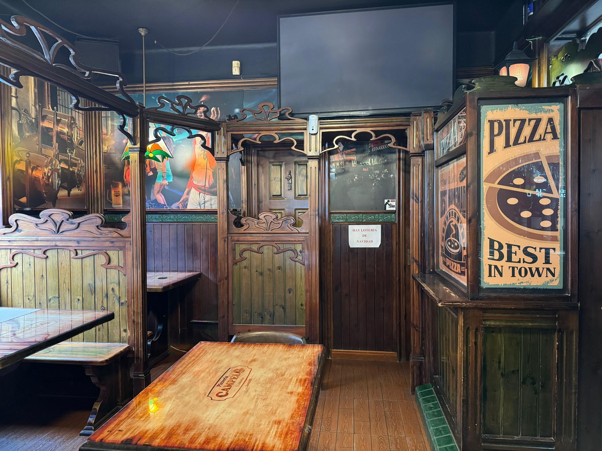 Interior de un pub con paneles de madera oscura, cabinas, un anuncio de pizza y una puerta.