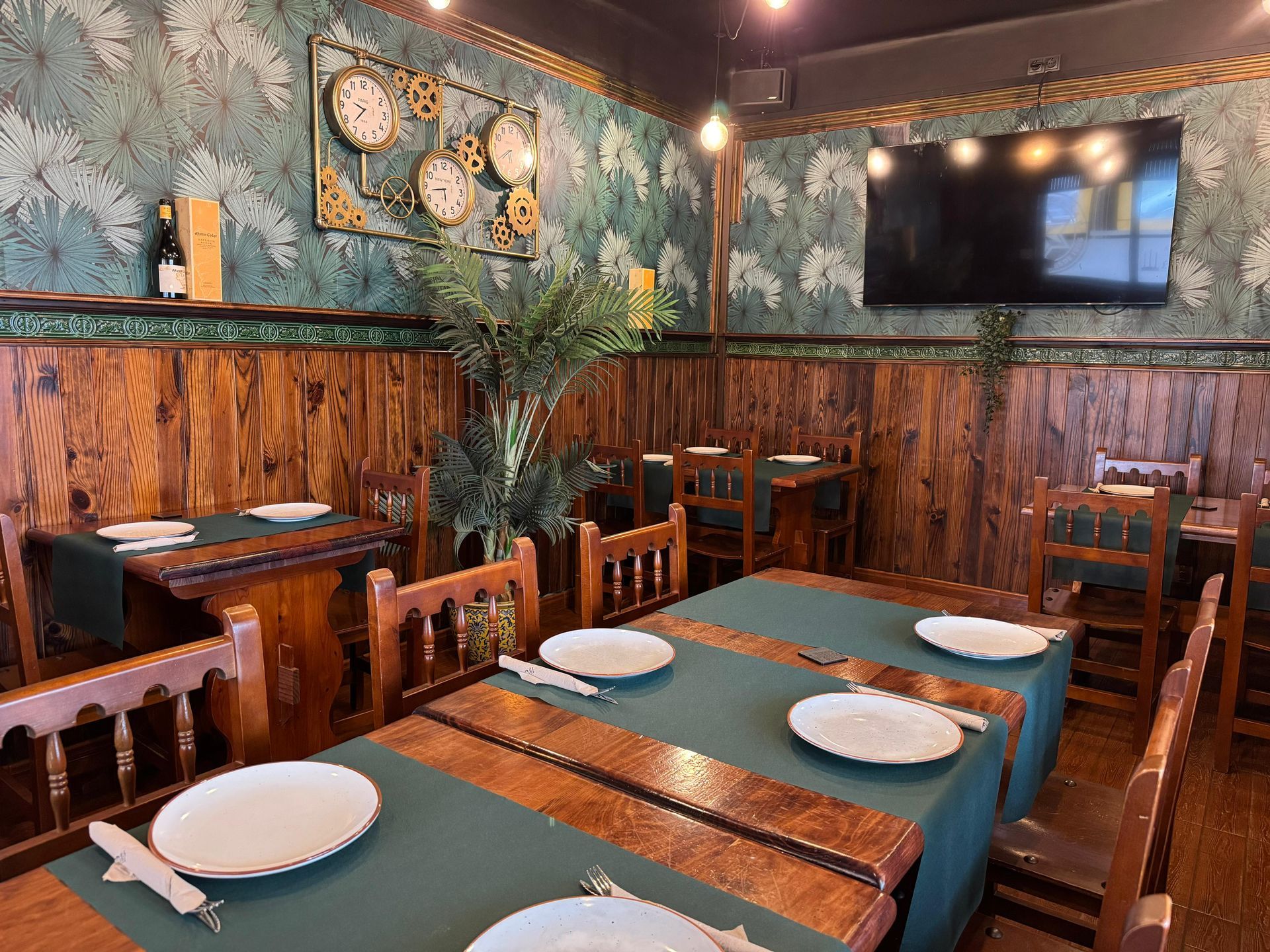 Interior de restaurante con paneles de madera, manteles verdes y arte decorativo de pared.