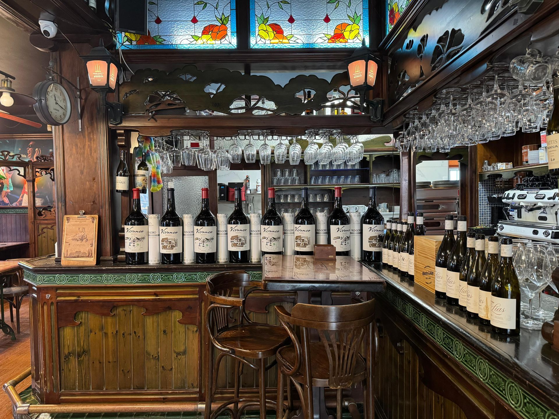 Interior de bar con botellas de vino, copas y detalles de madera ornamentados.