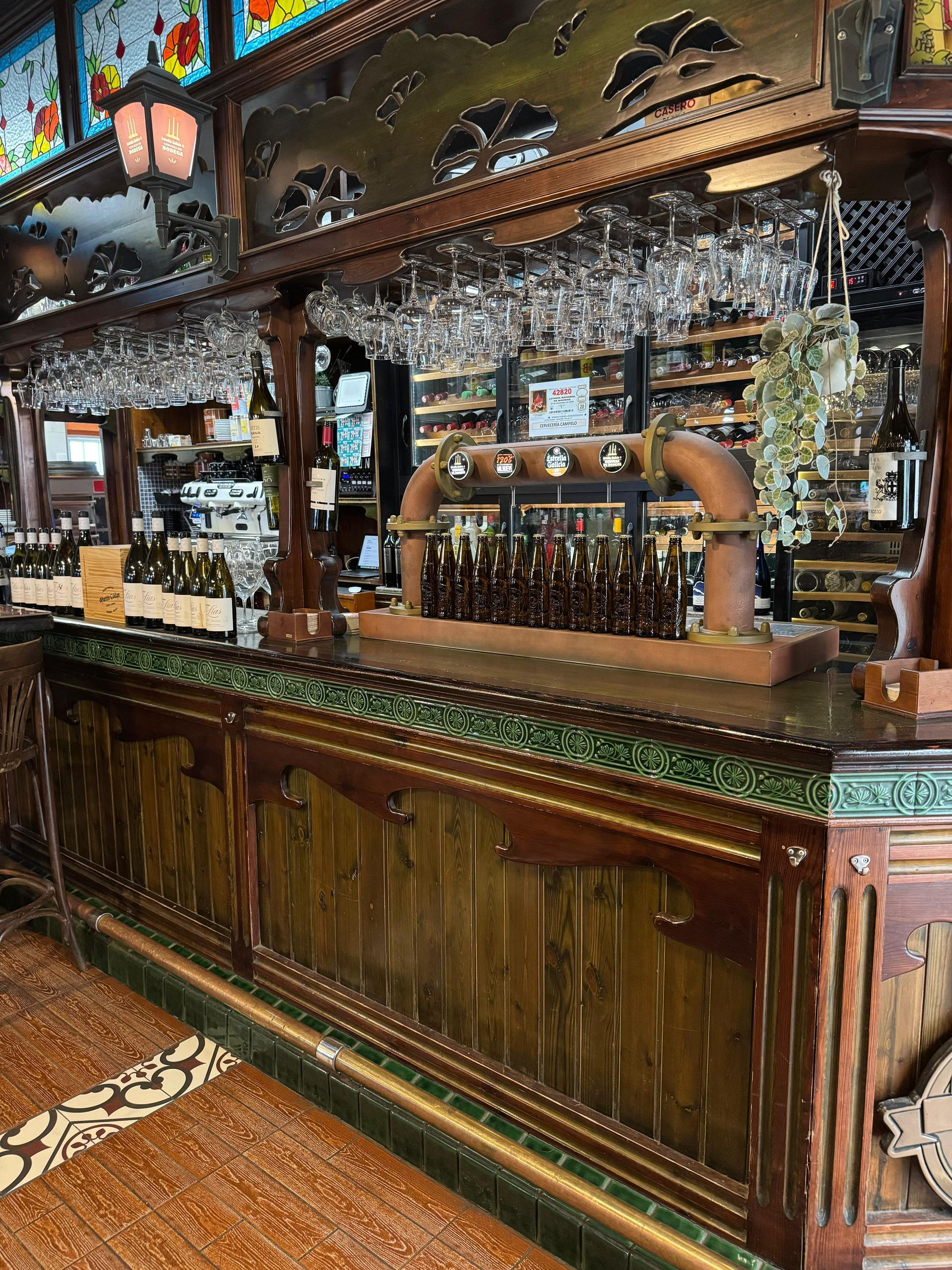 Interior de bar con paneles de madera, grifos de cerveza, copas de vino y botellas.