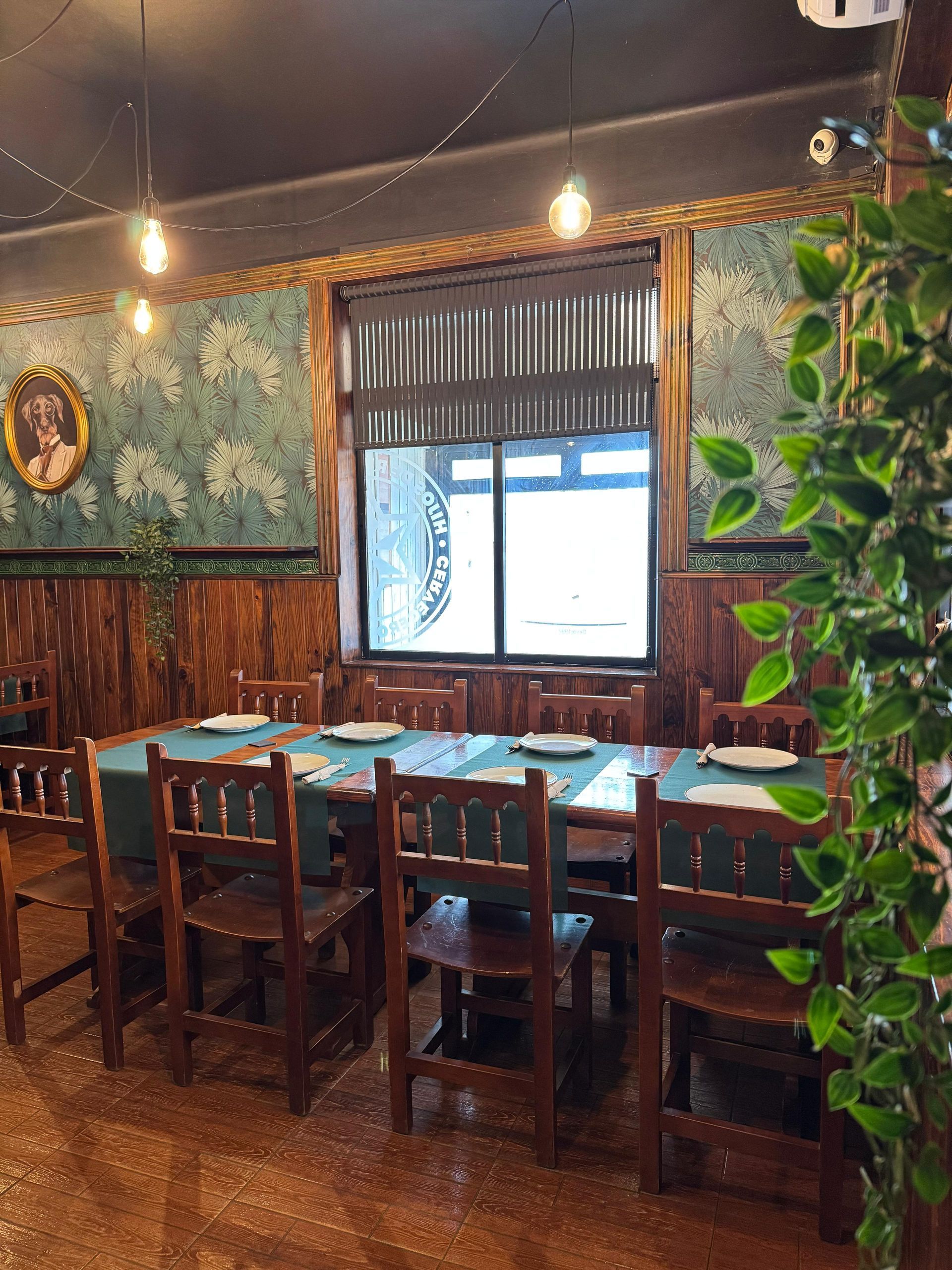 Un comedor con una mesa larga, sillas, ventana y papel tapiz ornamentado.