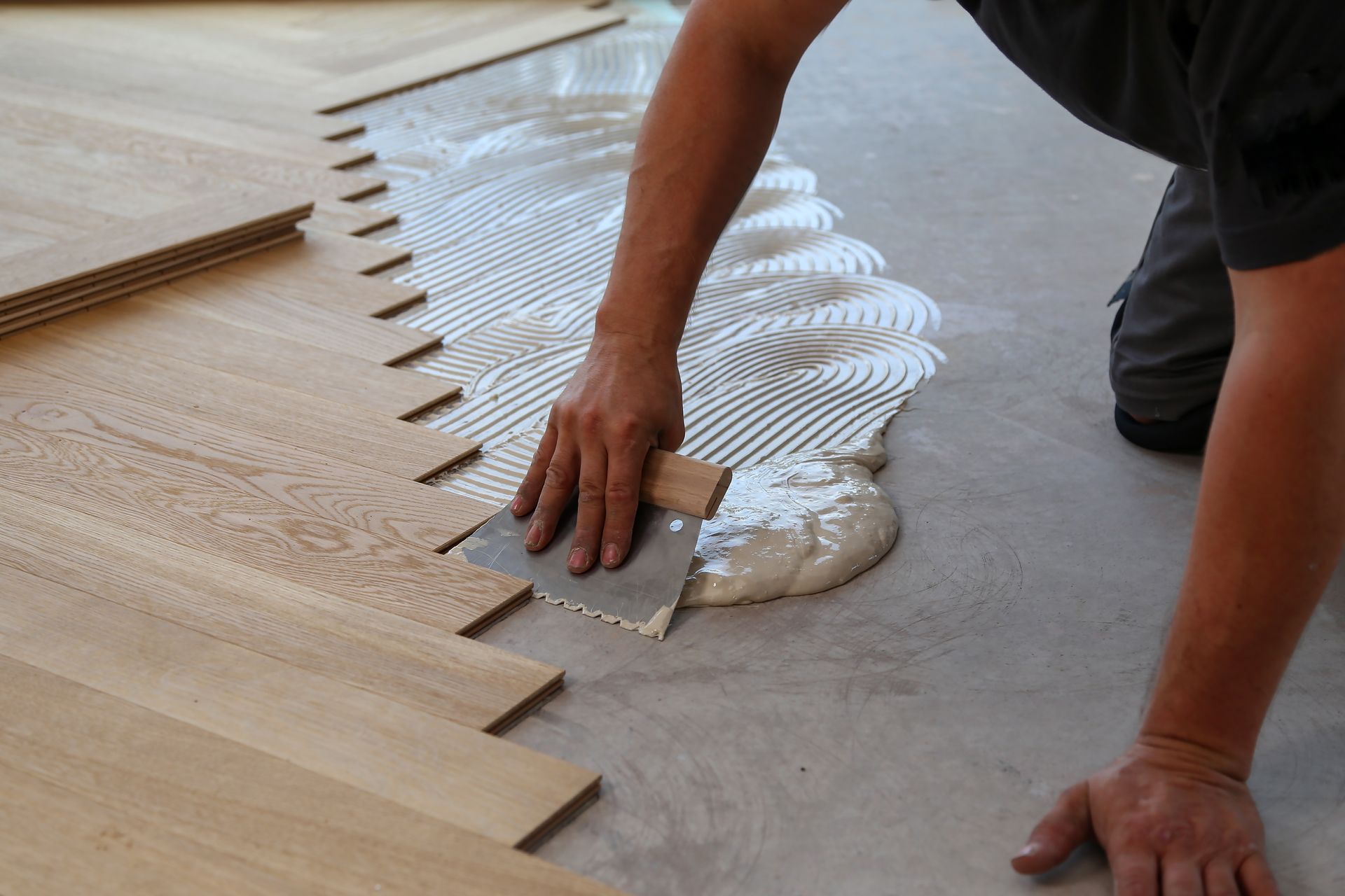 Mains appliquant de la colle à bois pour la pose de parquet