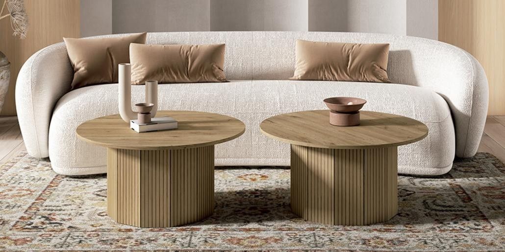 Sala de estar con un sofá curvo de color crema, dos mesas de centro redondas de madera y una alfombra estampada.