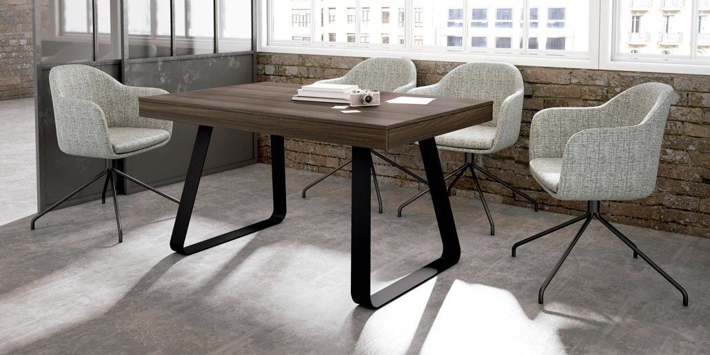 Una mesa de conferencias con cuatro sillas en una habitación con paredes de ladrillo y grandes ventanas.