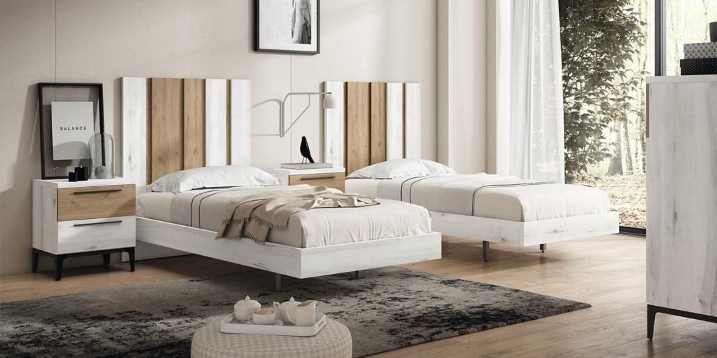 Dormitorio con dos camas individuales, mesitas de noche a juego y alfombra. Las camas tienen cabeceros blancos y de madera.