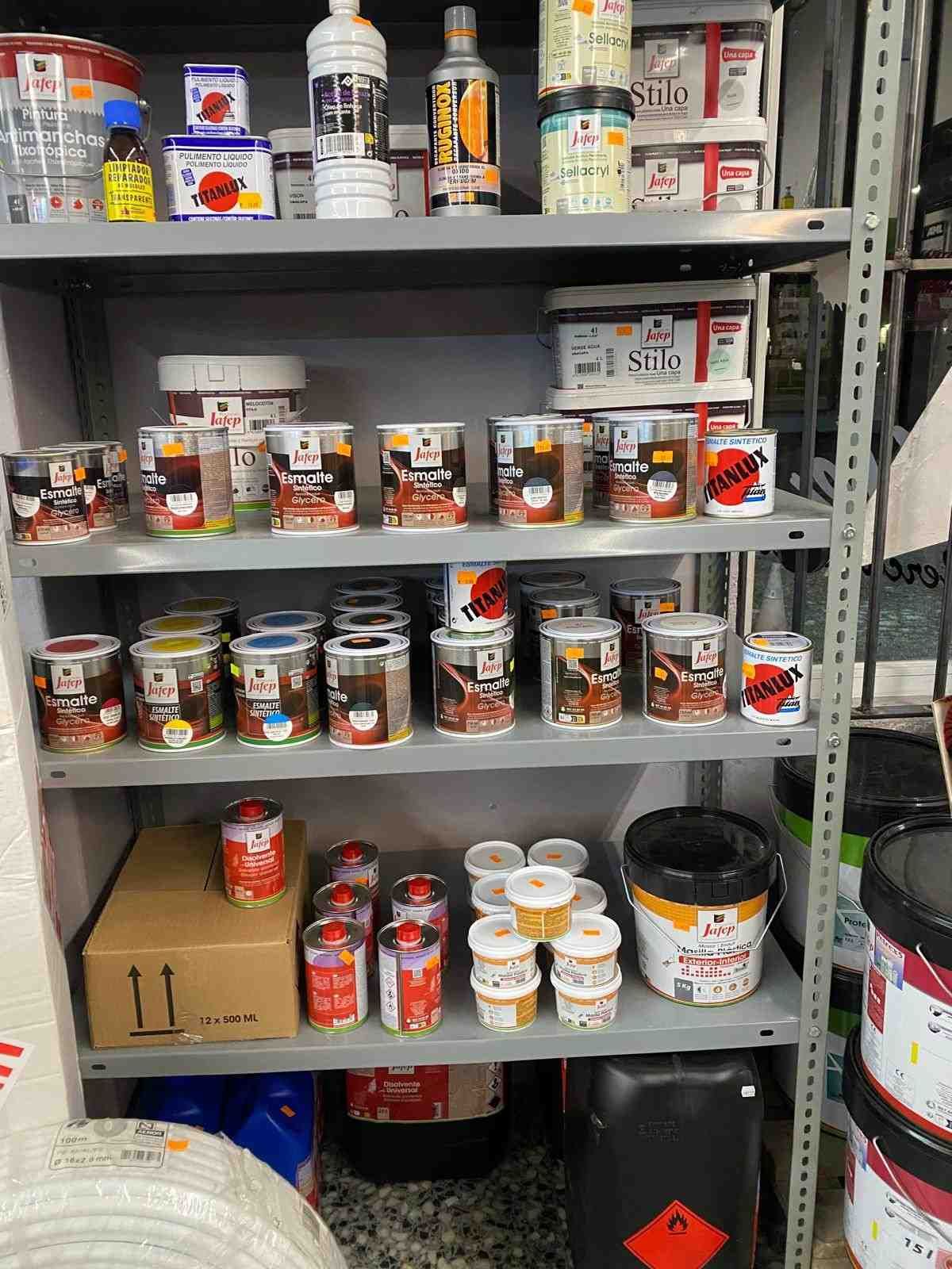 Estantes llenos de latas y botellas de pintura de varios colores, que muestran el inventario de una tienda de pinturas.