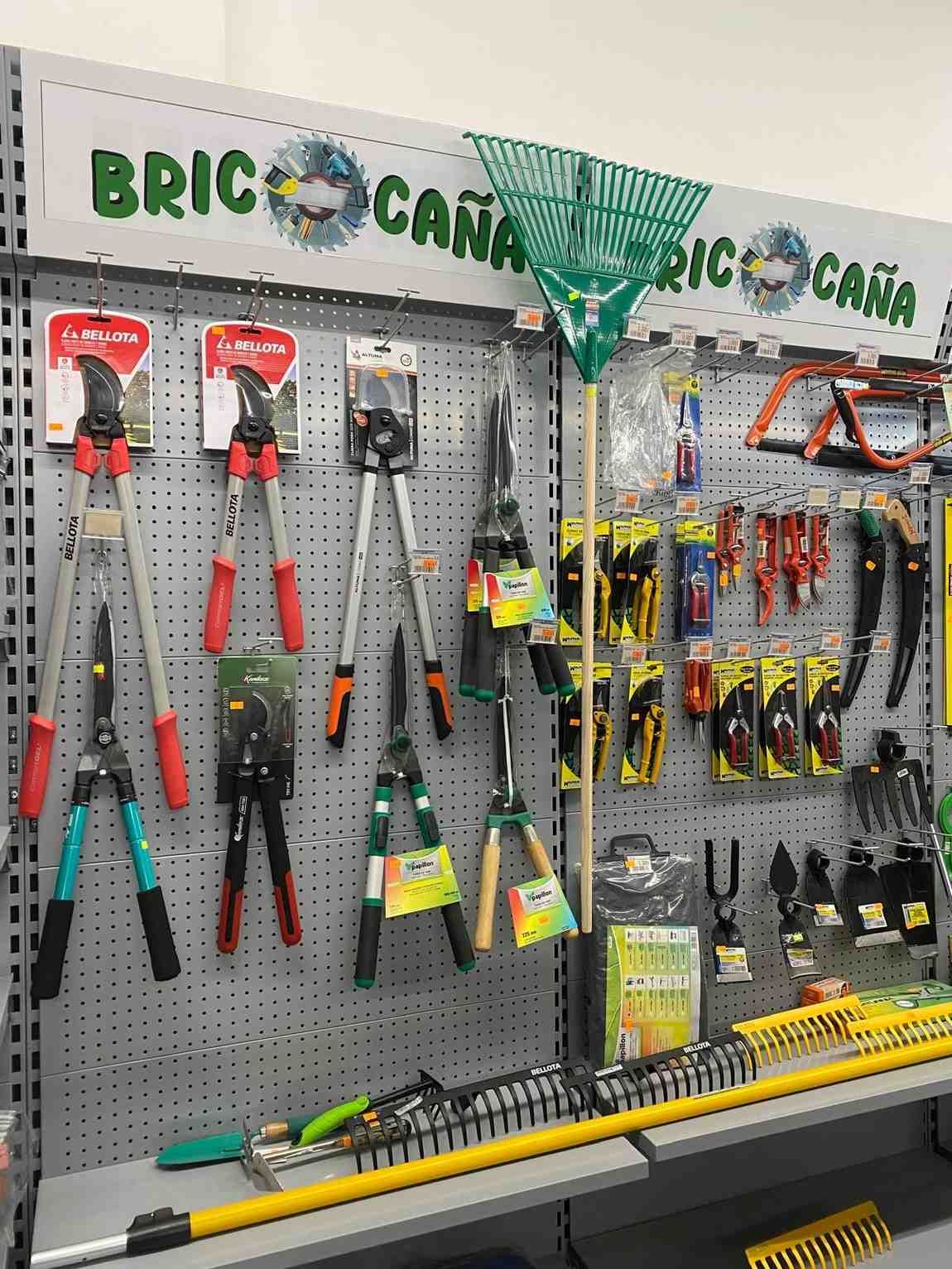 Exhibición de herramientas de jardinería en ferretería: podadoras, rastrillos, sierras, guantes y otros equipos.