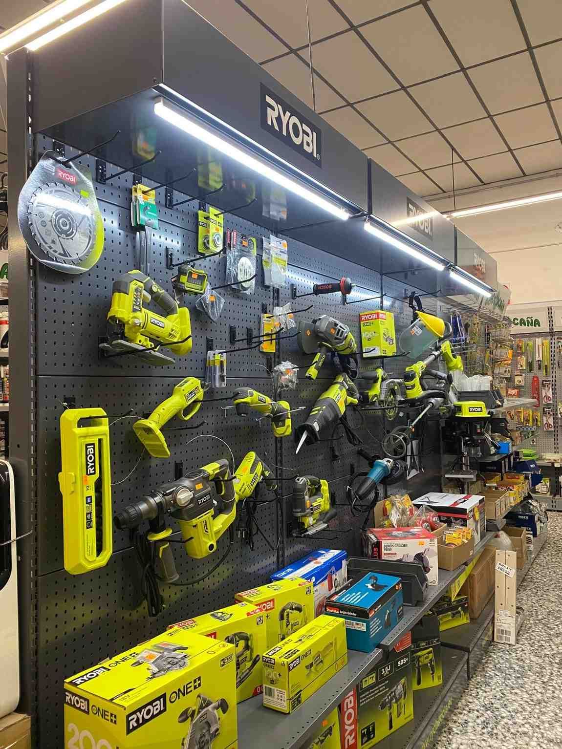Herramientas eléctricas Ryobi exhibidas en una pared de tablero perforado en una tienda, iluminadas con luces de techo.
