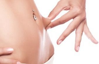 Una mujer con un piercing en el ombligo tiene las manos sobre el estómago.