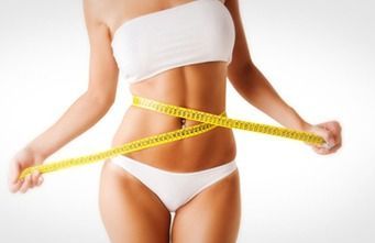 Una mujer en ropa interior blanca está midiendo su cintura con una cinta métrica.