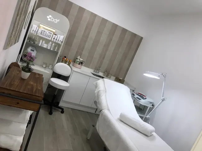 Sala de tratamientos de belleza con camilla facial, armarios blancos, espejo y papel pintado a rayas