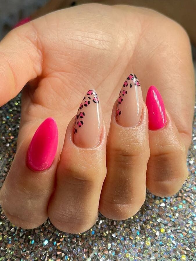 Un primer plano de la mano de una mujer con uñas rosas y un diseño de estampado de leopardo.