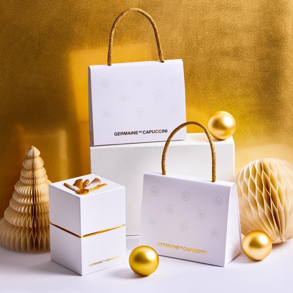 Tres bolsas blancas con asas doradas se apilan una encima de la otra.