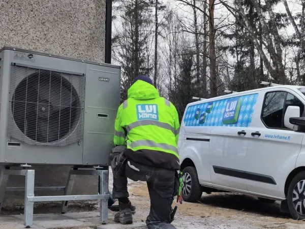 Neonvihreään takkiin pukeutunut työntekijä säätää ulkoilmanvaihtoyksikköä valkoisen pakettiauton vieressä lumisissa olosuhteissa