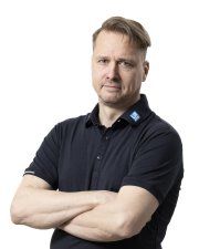 Mustassa poolopaidassa oleva henkilö seisoo kädet ristissä valkoista taustaa vasten