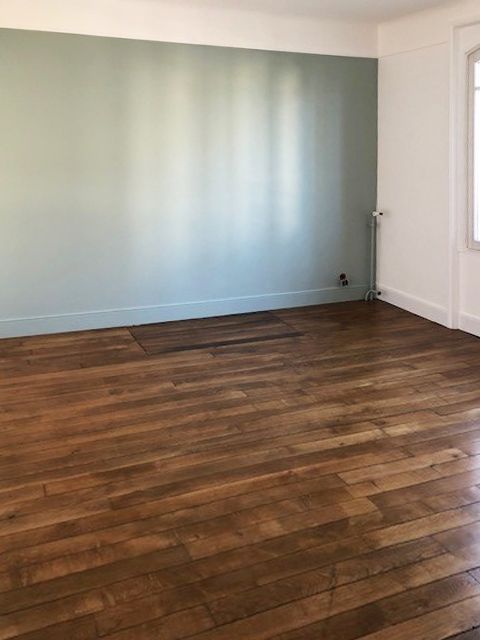 Pièce vide avec parquet, mur bleu et moulures blanches.