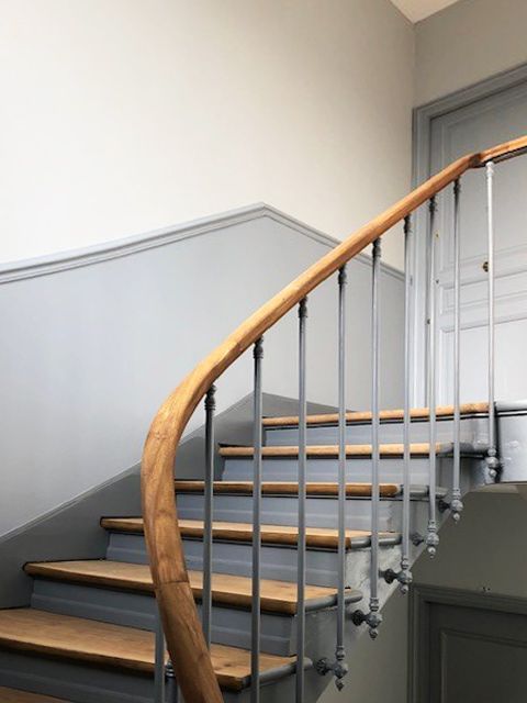 Escalier en bois avec rampe incurvée et balustres en métal. Murs gris.