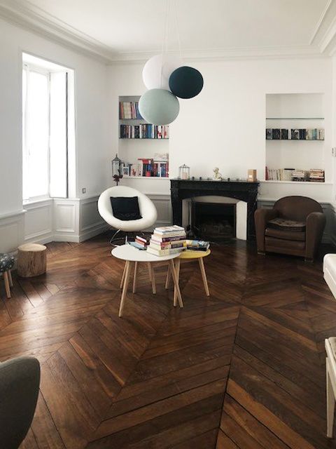 Salon avec parquet, cheminée et lampes suspendues colorées.