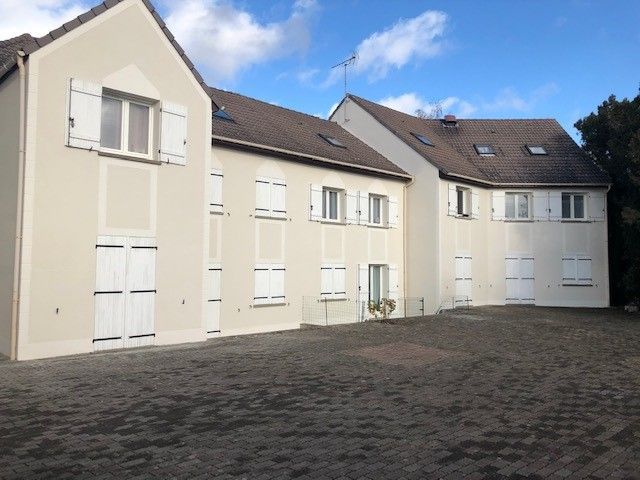 Immeuble beige à plusieurs étages avec des volets blancs se détachant sur un ciel bleu, toit marron.