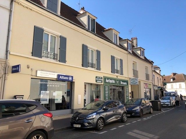 Rangée de boutiques, voitures garées dans la rue.