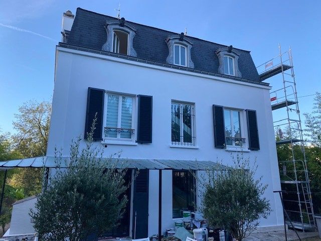 Maison blanche à deux étages avec volets noirs, toit sombre et échafaudages sur le côté.