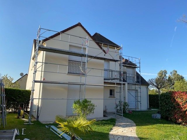 Maison à deux étages avec échafaudages pour travaux extérieurs sous un ciel bleu.