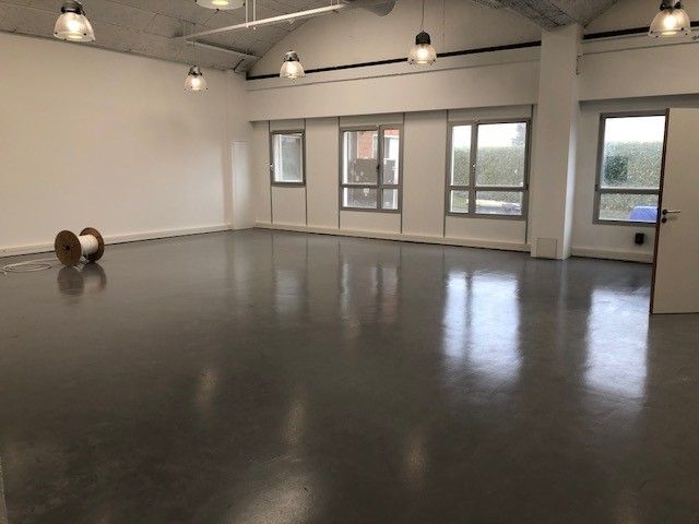 Pièce vide au sol gris, murs blancs, fenêtres et éclairage au plafond.