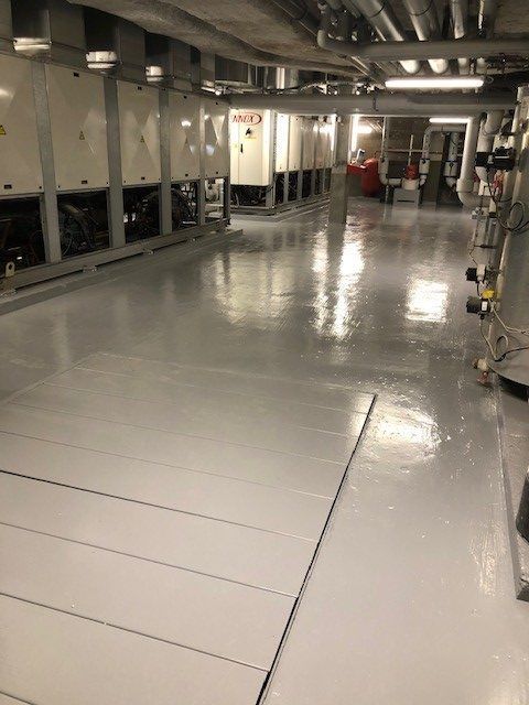 Un intérieur commercial avec un sol gris brillant, des équipements utilitaires et des canalisations aériennes.