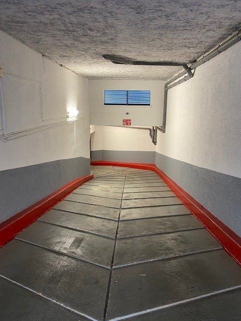 Rampe en béton aux murs gris, rouges et blancs menant à une petite fenêtre.