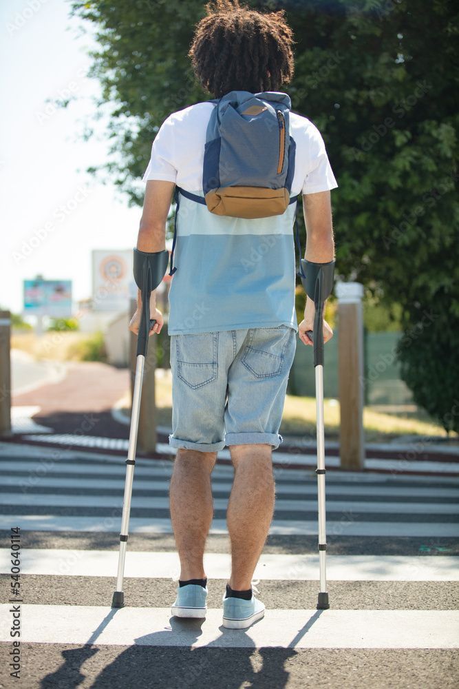 Un uomo con le stampelle e uno zaino sta attraversando la strada.