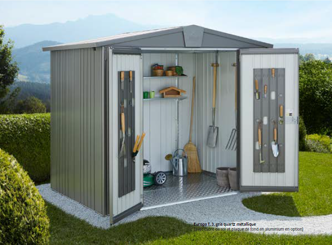 Abri de jardin en métal avec portes ouvertes, contenant des outils de jardin ; situé sur de l'herbe avec des montagnes en arrière-plan.