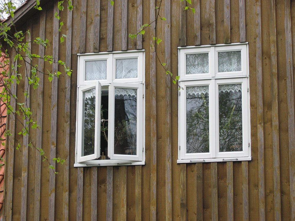 An der Seite eines Holzgebäudes befinden sich zwei weiße Fenster.
