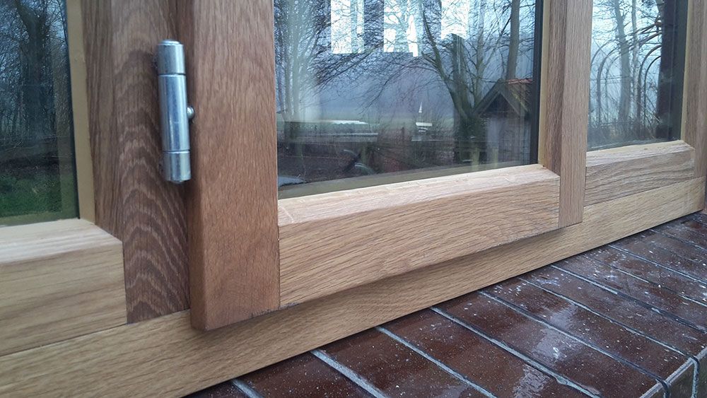 Auf einer Ziegelmauer sitzt ein hölzerner Fensterrahmen.