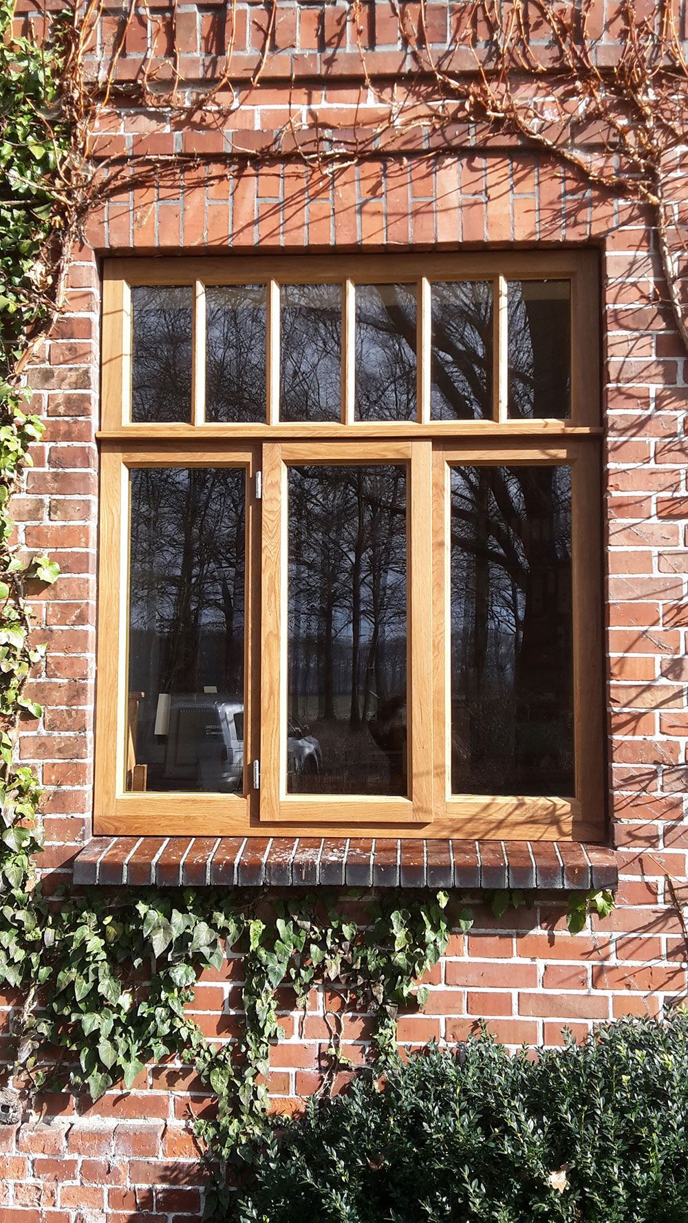 Ein Holzfenster an einer Ziegelwand, auf dem Efeu wächst