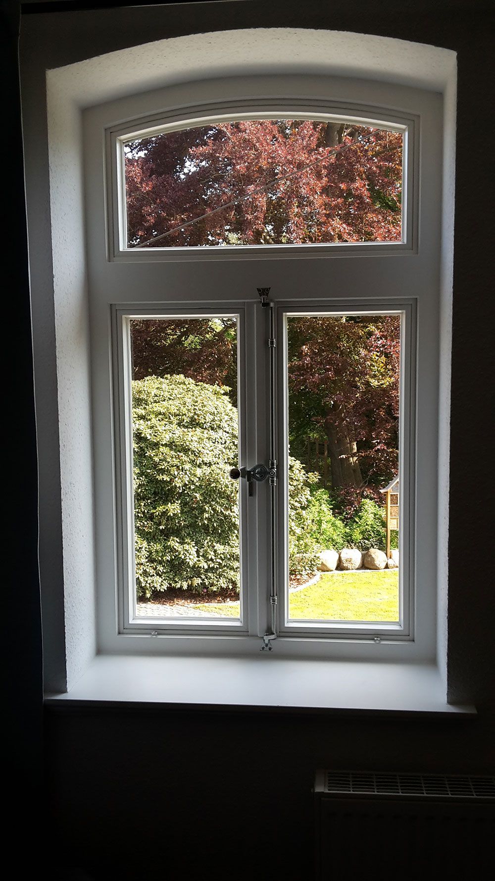 Ein weißes Fenster mit Blick auf einen Garten und Bäume.