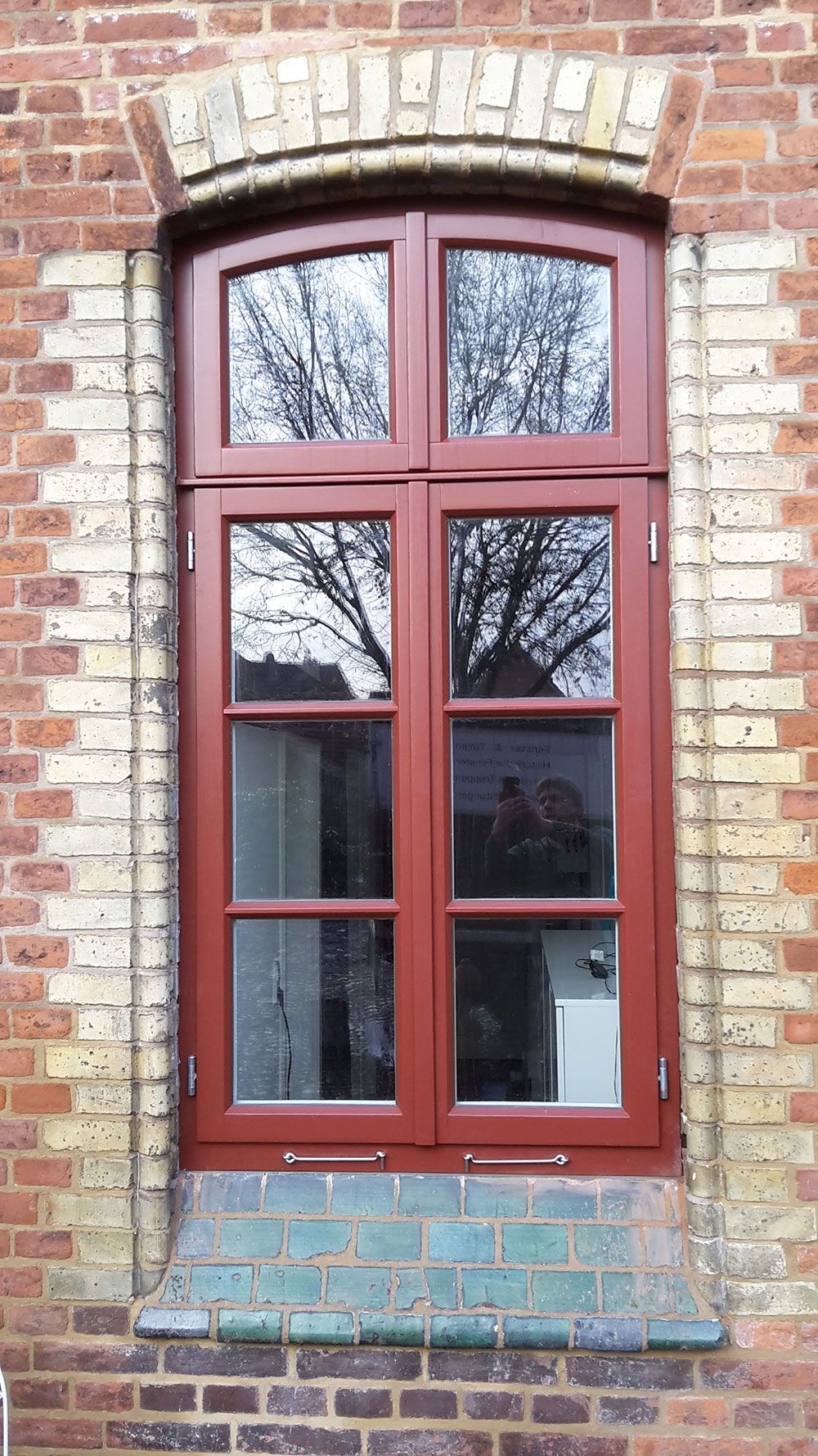 An einem Backsteingebäude befindet sich ein rotes Holzfenster.