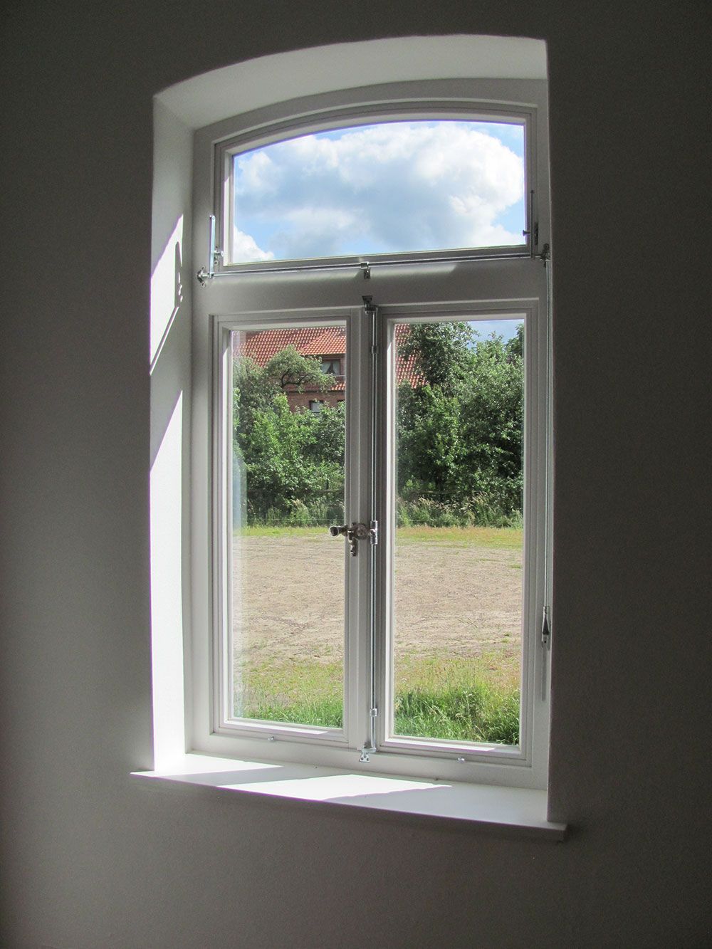 Ein weißes Fenster mit Blick auf ein Feld und Bäume.