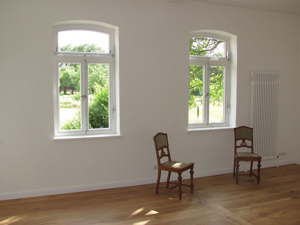 In einem leeren Raum mit zwei Fenstern stehen zwei Stühle.