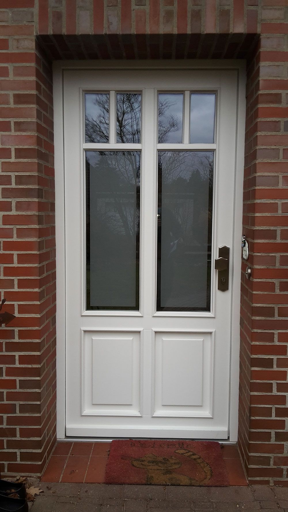 Eine weiße Haustür mit einer Backsteinmauer dahinter.