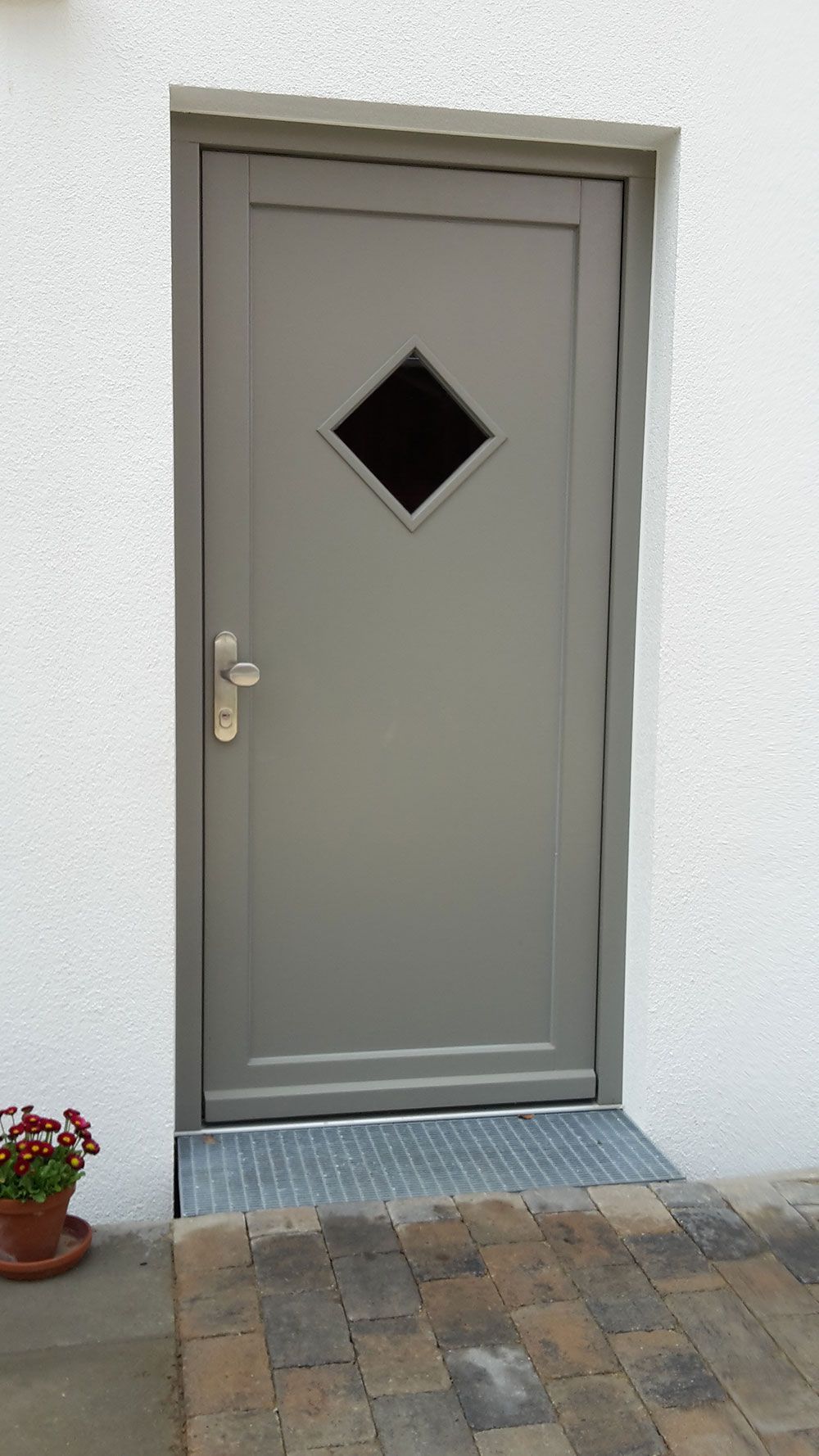 An einer weißen Wand befindet sich eine graue Tür mit einem rautenförmigen Fenster.