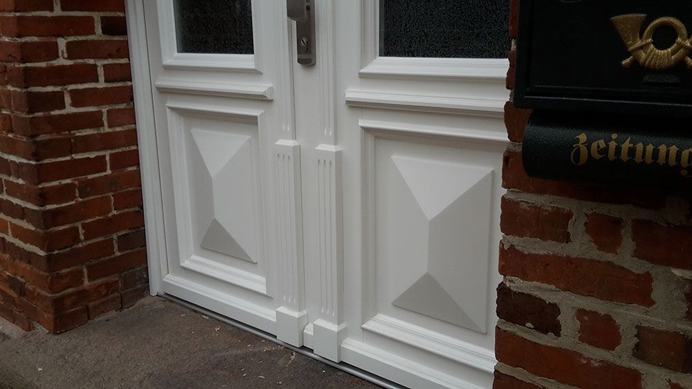 An einer Backsteinmauer befindet sich neben einem schwarzen Briefkasten eine weiße Tür.