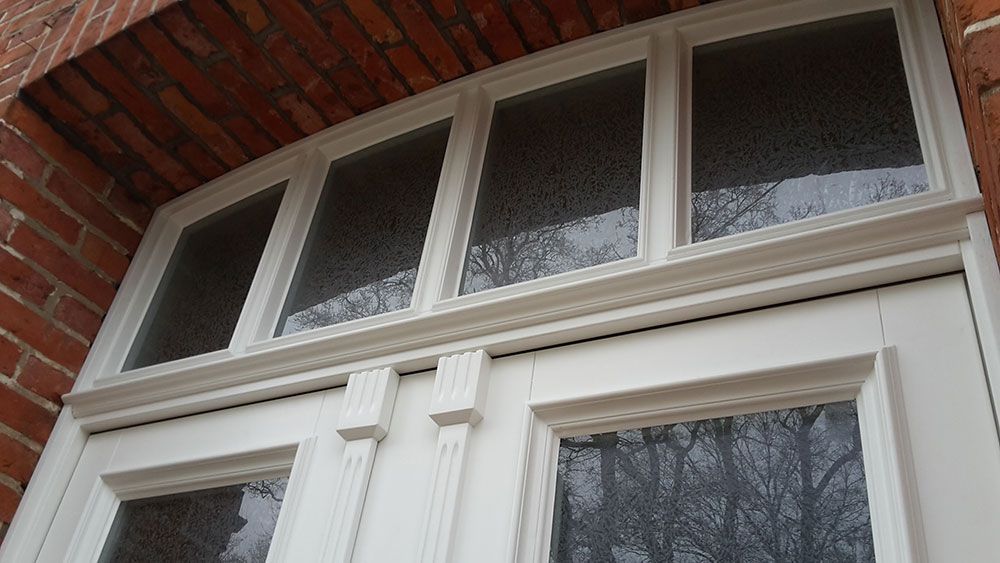 Eine weiße Tür mit drei Fenstern an einem Backsteingebäude.