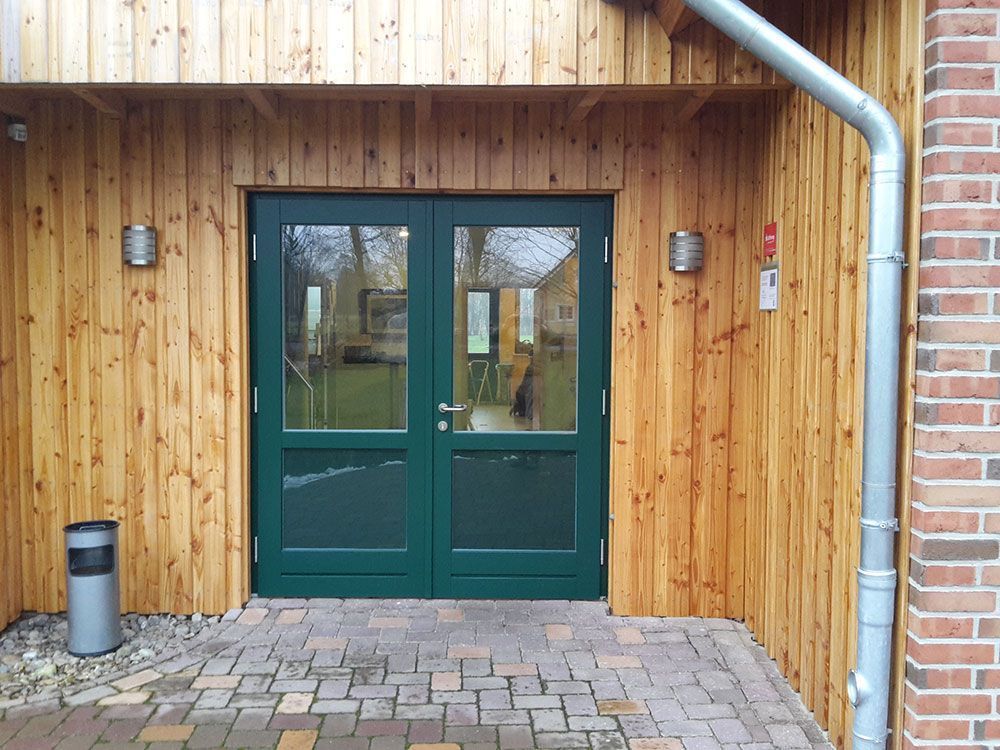 Ein Holzgebäude mit einer grünen Tür und einer Ziegelwand