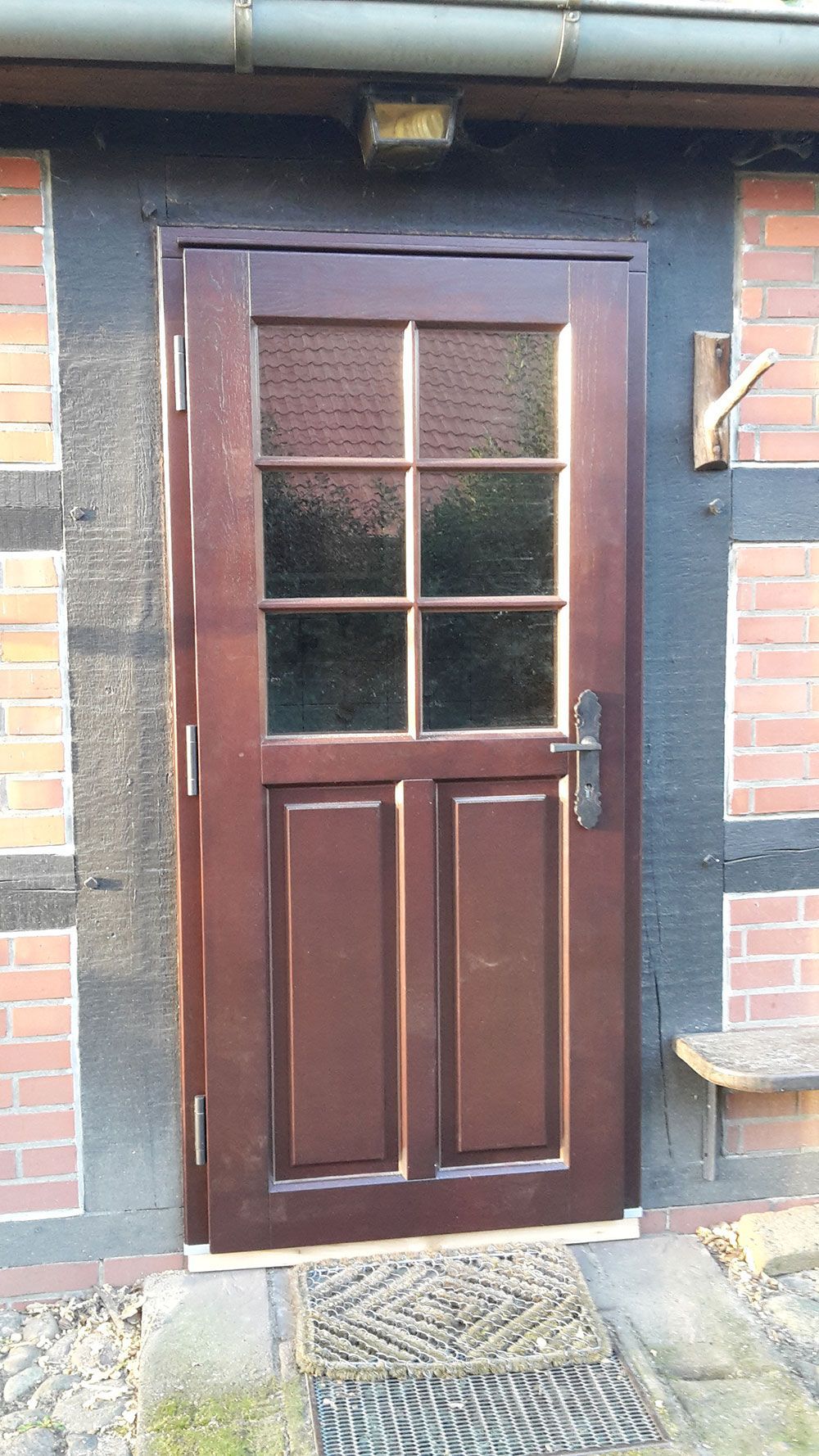An einem Backsteingebäude befindet sich eine Holztür mit einem Glasfenster.