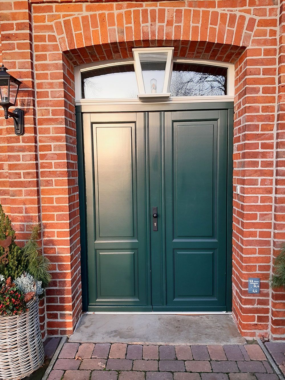 Vor einem roten Backsteingebäude befindet sich eine grüne Tür.