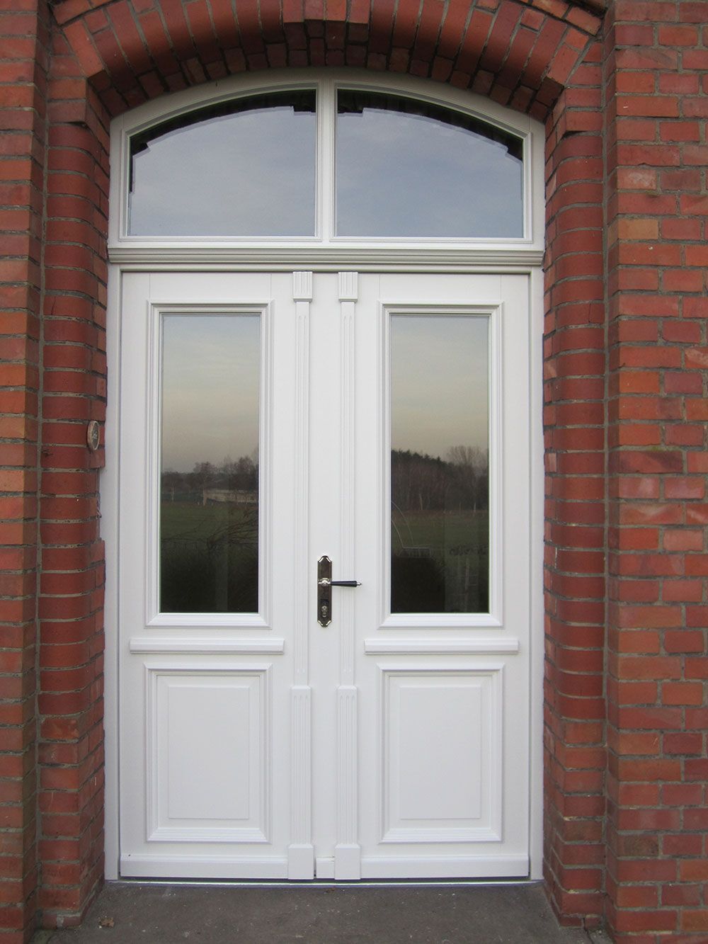 Eine weiße Tür mit zwei Fenstern an einem roten Backsteingebäude.
