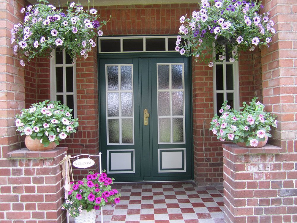 Ein Backsteingebäude mit einer grünen Tür und Blumen auf der Veranda
