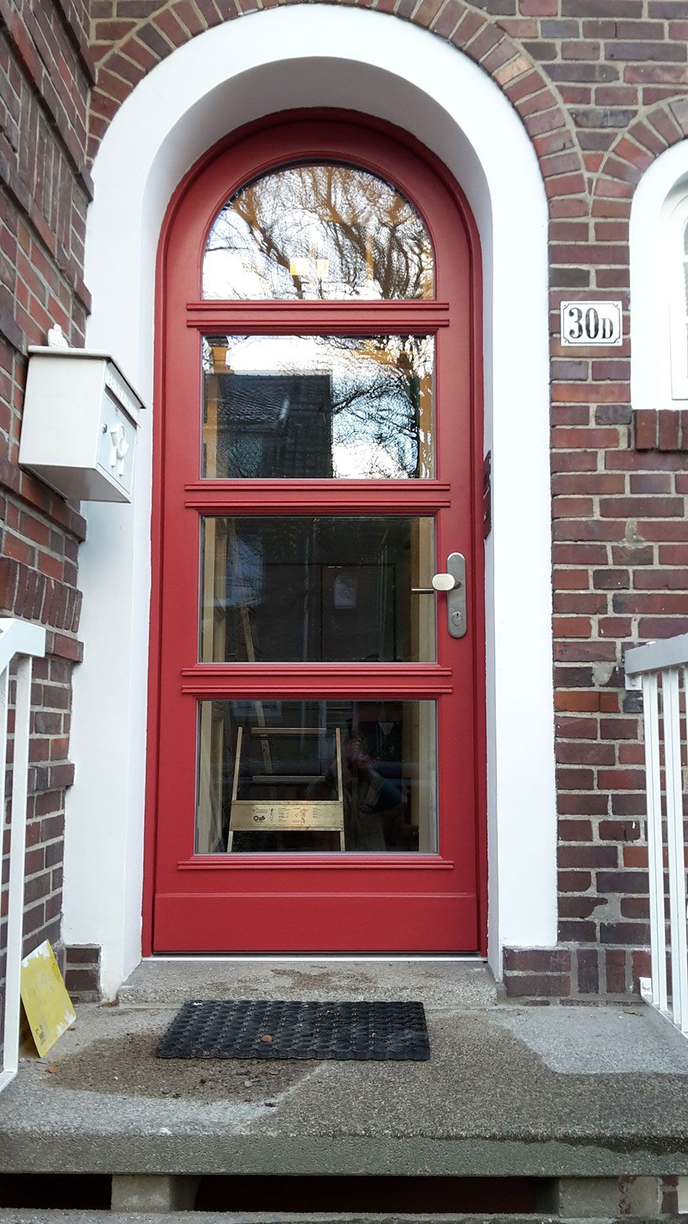 An einem Backsteingebäude befindet sich eine rote Tür mit weißem Rand.